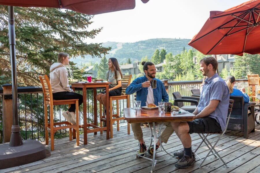 People sitting at tables on the deck of an outdoor restaurant in the mountains on a sunny summer day