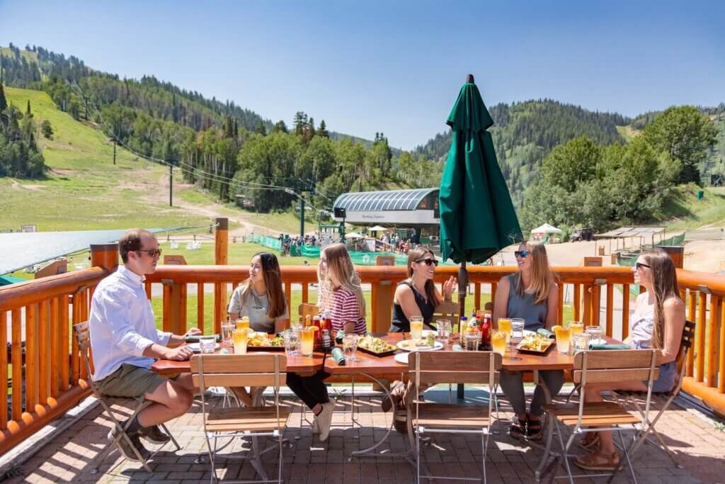 A group of people sitting at a table on an outdoor patio with a mountain view