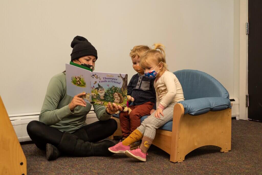 Adult reading a book to two toddlers during daycare