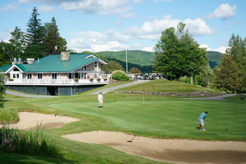 View of a mountain golf course with a restaurant and sundeck overlooking the green